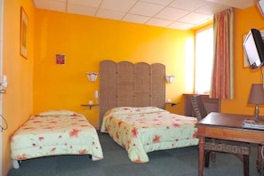 A room with two beds, a desk, a chair, a television, and a window with curtains.