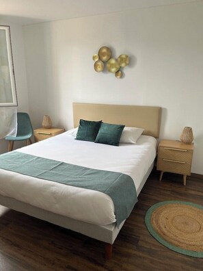 Een keurig opgemaakt slaapkamer met een bed, nachtkastjes, een stoel en een decoratief object aan de muur.