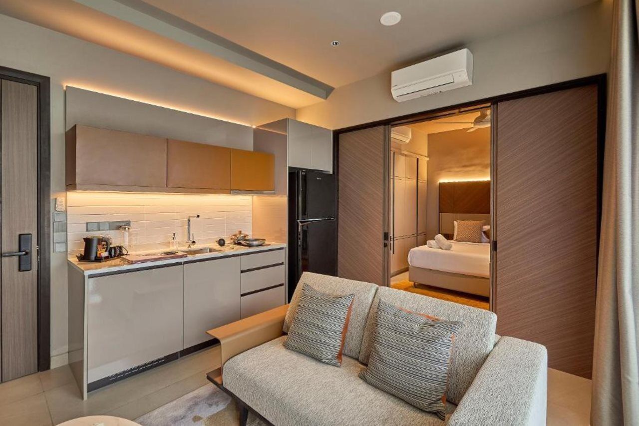 A compact hotel room with a kitchenette, a sofa, and a sliding door leading to a bathroom.
