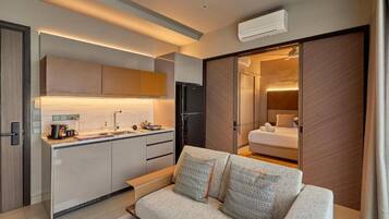 A compact hotel room with a kitchenette, a sofa, and a sliding door leading to a bathroom.