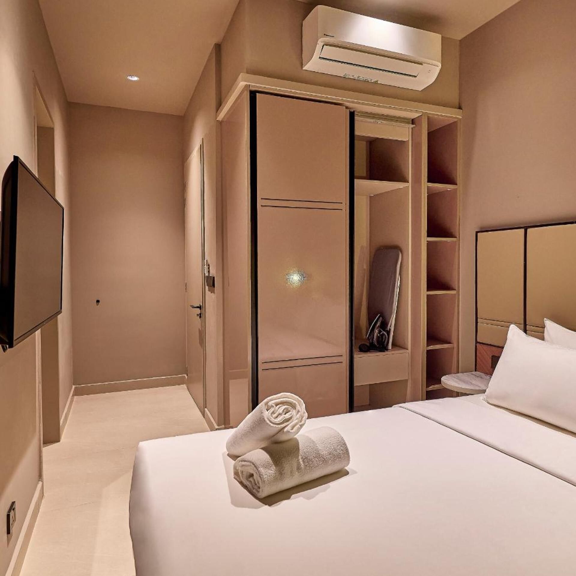 A hotel room with a bed, a wardrobe, a mirror, and an air conditioning unit.