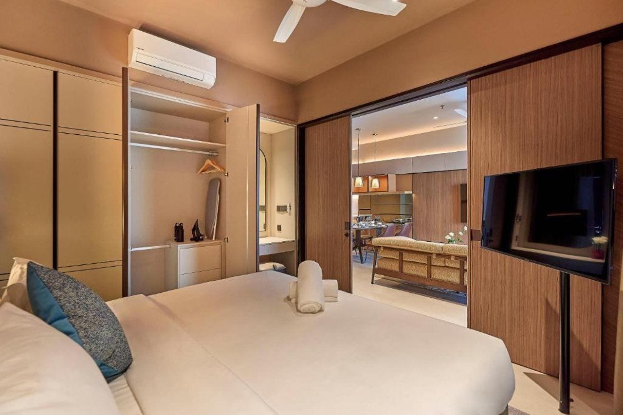 A hotel room with a bed, a TV, a wardrobe, and a view into the kitchen area.