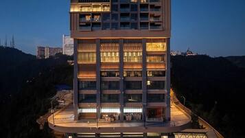 A multi-story hotel with a curved rooftop terrace, surrounded by hills and other buildings.