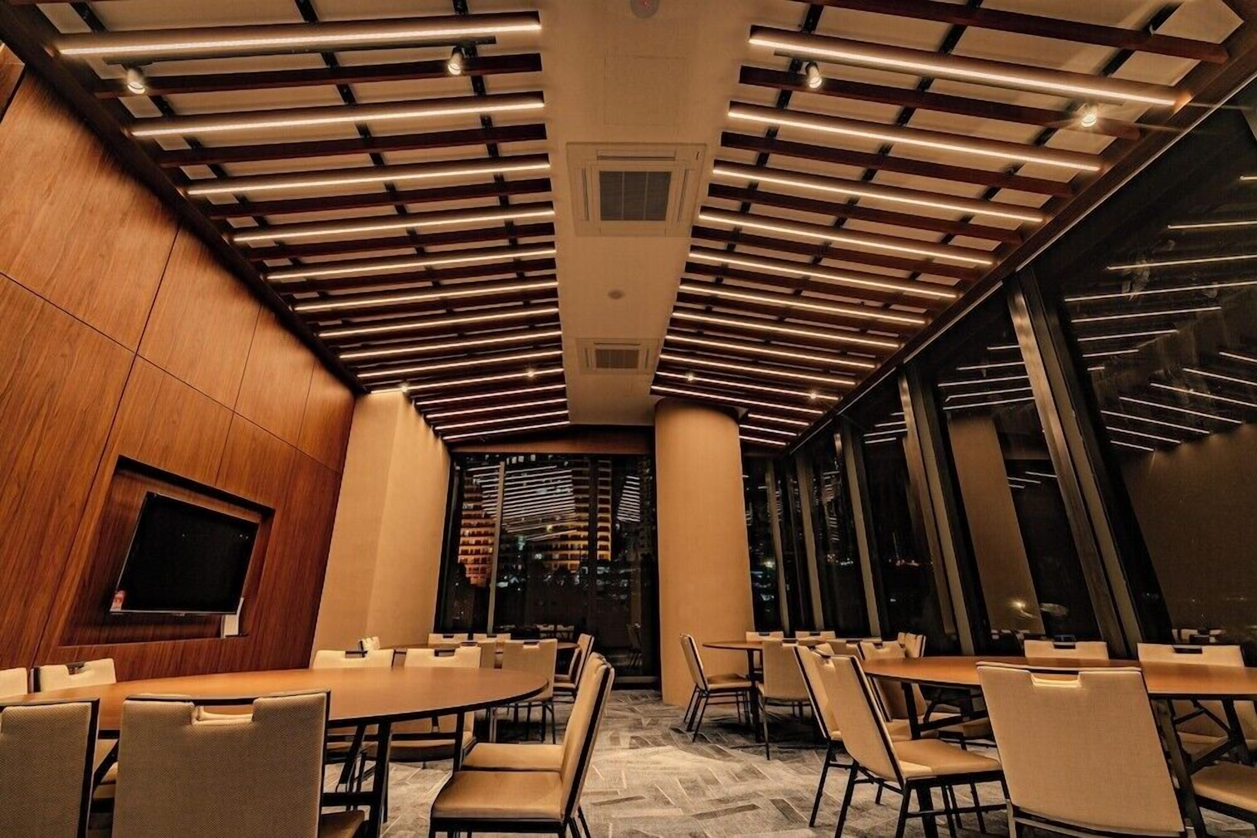 A conference room with a modern ceiling design, large windows, and a flat-screen TV.
