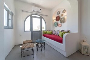 A modern living room with a white sofa, a glass table, wicker chairs, decorative plates on the wall, and a white lantern. - Black Coast Hotel (Santorini)