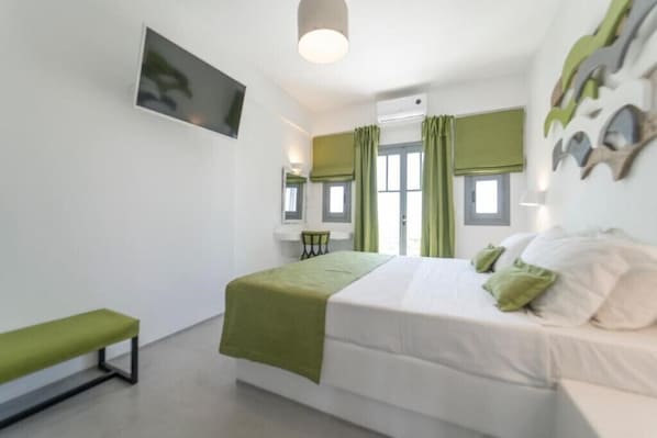 Ein Schlafzimmer mit Bett, einer Bank, einem Schreibtisch und einem Fenster mit Vorhängen.