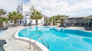 En swimmingpool med solstolar och palmer, en vit byggnad med ett torn och en klar himmel.