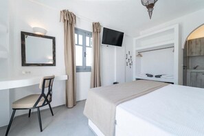 A bedroom with a bed, a desk with a chair, a television, and a wardrobe. - Black Coast Hotel (Santorini)