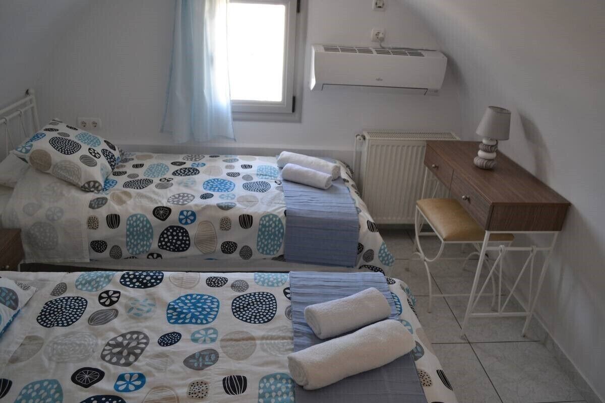 A twin room with two beds, a desk, a chair, an air conditioning unit, and a window with curtains.