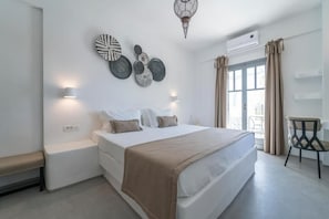 Un dormitorio moderno con una cama grande, lámparas de noche, detalles decorativos en la pared y vistas al exterior a través de una puerta corredera.