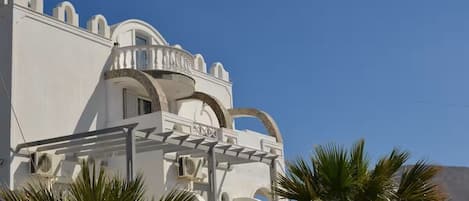 A white building with arched windows and balconies, surrounded by palm trees.