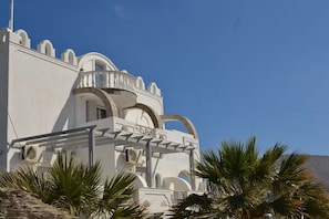 Un edificio blanco con ventanas arqueadas y balcones, rodeado de palmeras.