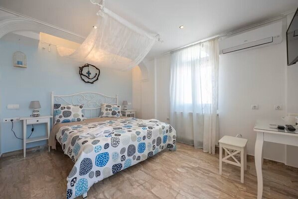 A bedroom with a bed, bedside tables, a desk, and a chair. - Black Coast Hotel (Santorini)