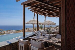 An outdoor seating area with a pool, umbrellas, and a view of the sea. - Maximus Mykonos Adults Only (Mykonos)