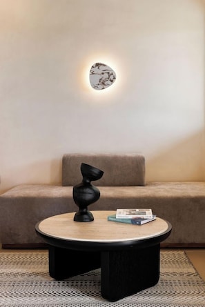 A modern living room with a round coffee table, a black abstract sculpture, a cushion, and a wall-mounted light fixture. - Maximus Mykonos Adults Only (Mykonos)