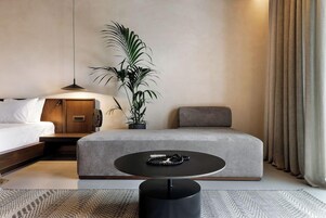 Una habitación de hotel moderna con cama, sofá, una mesa redonda y una planta en maceta.