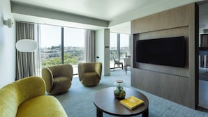 A modern hotel room with a large TV, comfortable seating, and a view of the city. - Altis Porto (Porto)