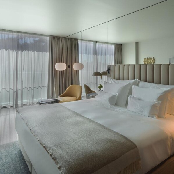 A modern hotel room with a large bed, a seating area with a chair, and a view through sheer curtains. - Altis Porto (Porto)