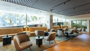 A modern lounge area with seating and tables, large windows, and a wooden floor. - Altis Porto (Porto)