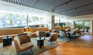 A modern lounge area with seating and tables, large windows, and a wooden floor. - Altis Porto (Porto)