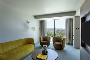 A modern hotel room with a sofa, two armchairs, a round coffee table with a book, a floor lamp, and a large window with curtains. - Altis Porto (Porto)