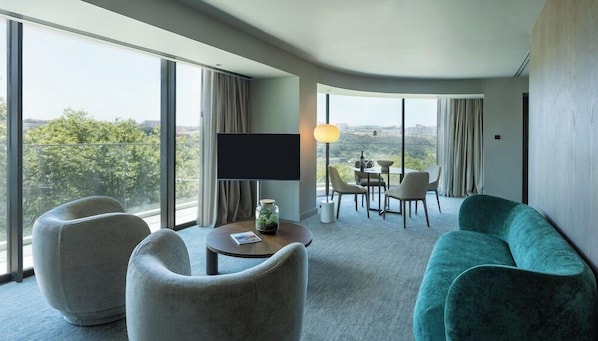 A modern hotel room with a large window, a flat-screen TV, a sofa, and a dining area with chairs and a table. - Altis Porto (Porto)