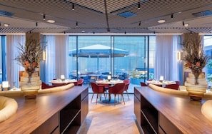 A modern hotel lobby with a central dining area, large windows, and decorative plants. - Altis Porto (Porto)