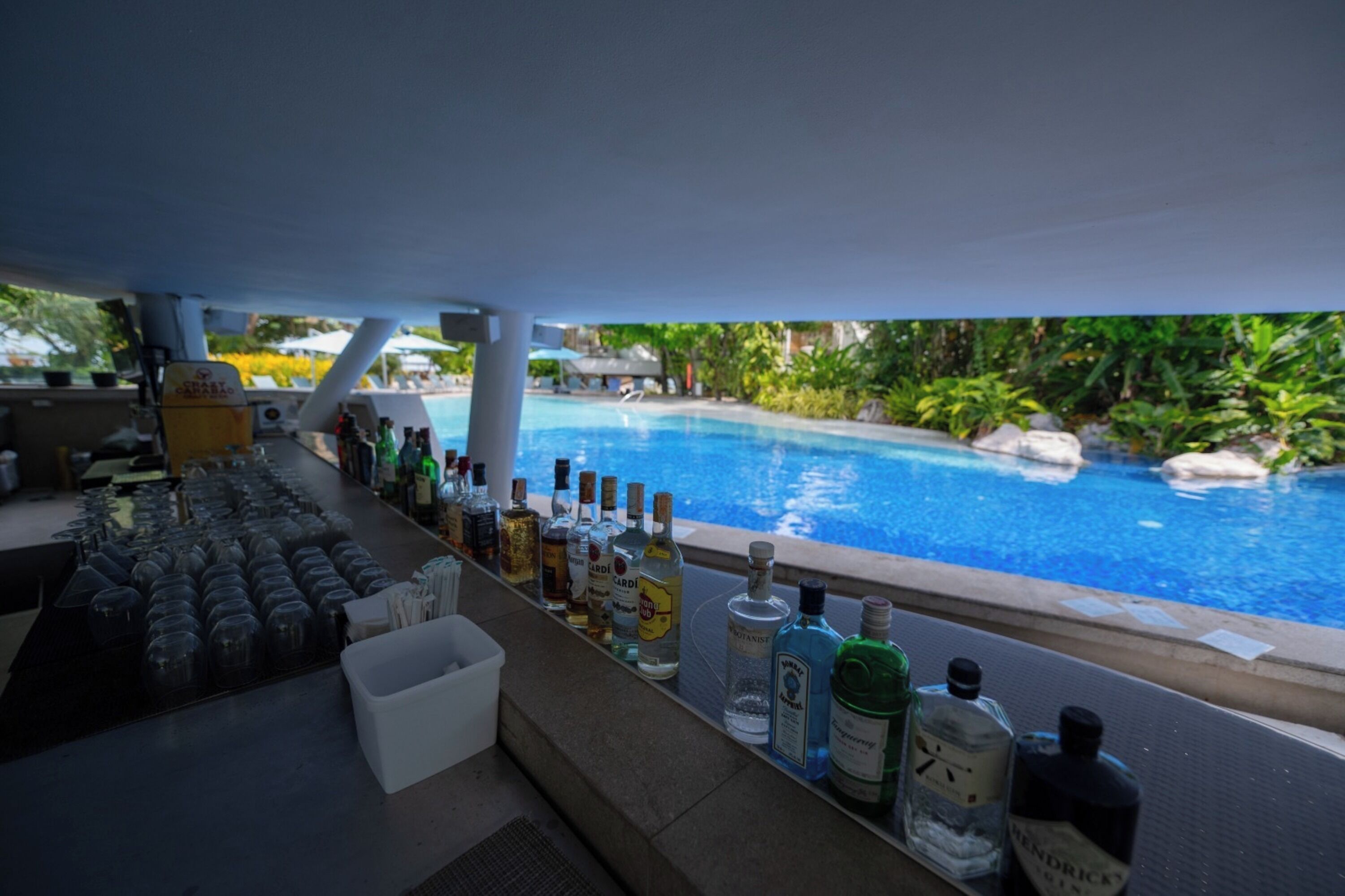 Angolo bar con vista sulla piscina, con diverse bottiglie e bicchieri.