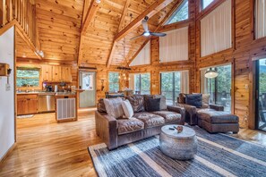 A cabin interior with a wooden ceiling, a kitchen area, a seating area with a sofa and armchairs, and large windows. - Aska Adventure Area - Hot Tub- Sunset Views - Pets (Cherry Log)
