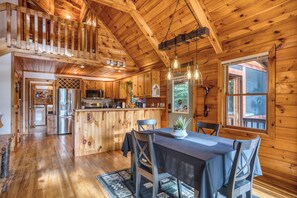 A wooden cabin interior with a dining area, kitchen, and a loft bedroom. - Aska Adventure Area - Hot Tub- Sunset Views - Pets (Cherry Log)