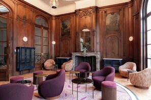A lobby with ornate wood paneling, a fireplace, and modern seating.