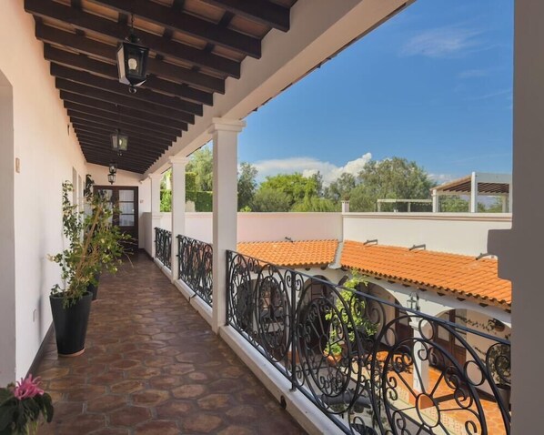A covered balcony with a stone floor, black wrought iron railing, and potted plants. - Iraola Hotel Boutique (Salta)