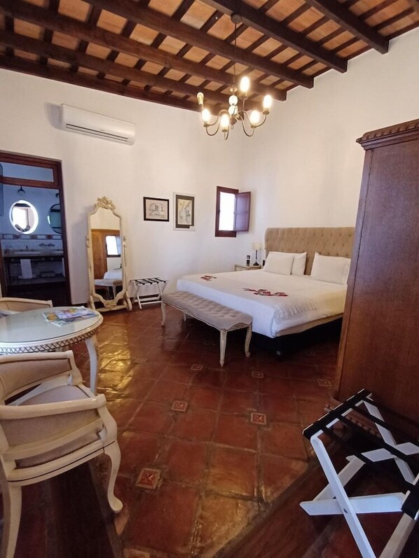 A bedroom with a bed, a bedside table, a chair, a mirror, and a chandelier. - Iraola Hotel Boutique (Salta)