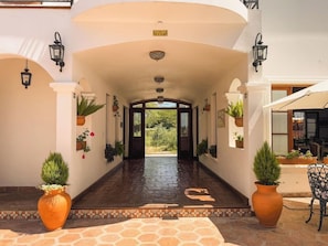L’entrée d’un hôtel, avec un couloir central, des plantes en pot et un panneau indiquant la sortie.