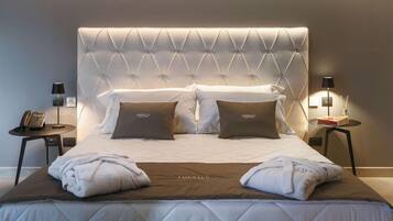 A hotel room with a tufted headboard, two bedside tables with lamps, a bed with white bedding and two pillows, and a brown throw blanket.