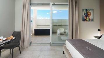 Quarto de hotel com cama, mesa de jantar com prato de comida, cadeira, quadro na parede e porta de vidro deslizante para uma varanda.