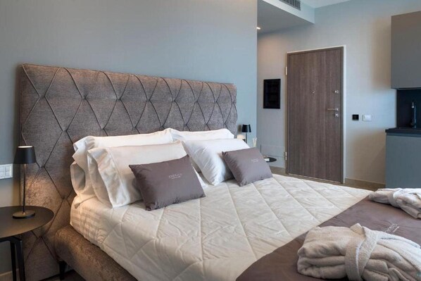 A hotel room with a large bed, a headboard, a bedside table with a lamp, a wardrobe, and a bathroom area.