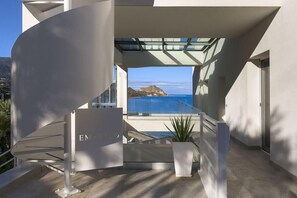 A modern architectural design with a staircase leading to a balcony overlooking a coastal view.