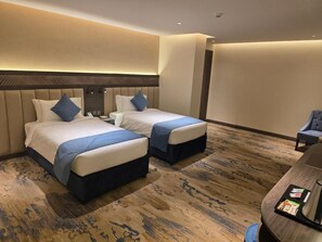 A hotel room with two beds, a desk, and a chair.