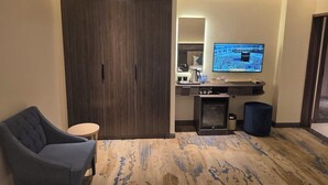 A hotel room with a large wardrobe, a flat-screen TV mounted on the wall, a small round table, and a blue chair. - Sedra Al Aalami Hotel (Madinah)