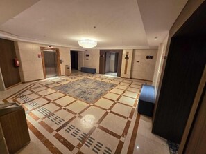 A hotel lobby with a check-in counter, elevators, a patterned carpet, and a chandelier. - Sedra Al Aalami Hotel (Madinah)