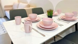 A dining table set with pink cups, bowls, and plates, with a small plant on the table. - Mossaz Suites by Mykey Global (Kuala Lumpur)