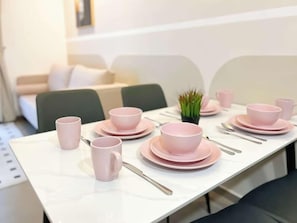 Una mesa de comedor dispuesta con tazas, cuencos y platos rosas, con una pequeña planta encima.