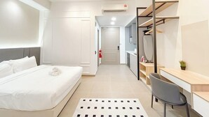 A modern hotel room with a bed, a desk, and a chair. There is a wardrobe with a mirror and a shelf with items on it. - Mossaz Suites by Mykey Global (Kuala Lumpur)