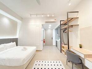 Una habitación de hotel moderna con cama, escritorio y silla. Se ve un armario con espejo y una estantería con objetos encima.
