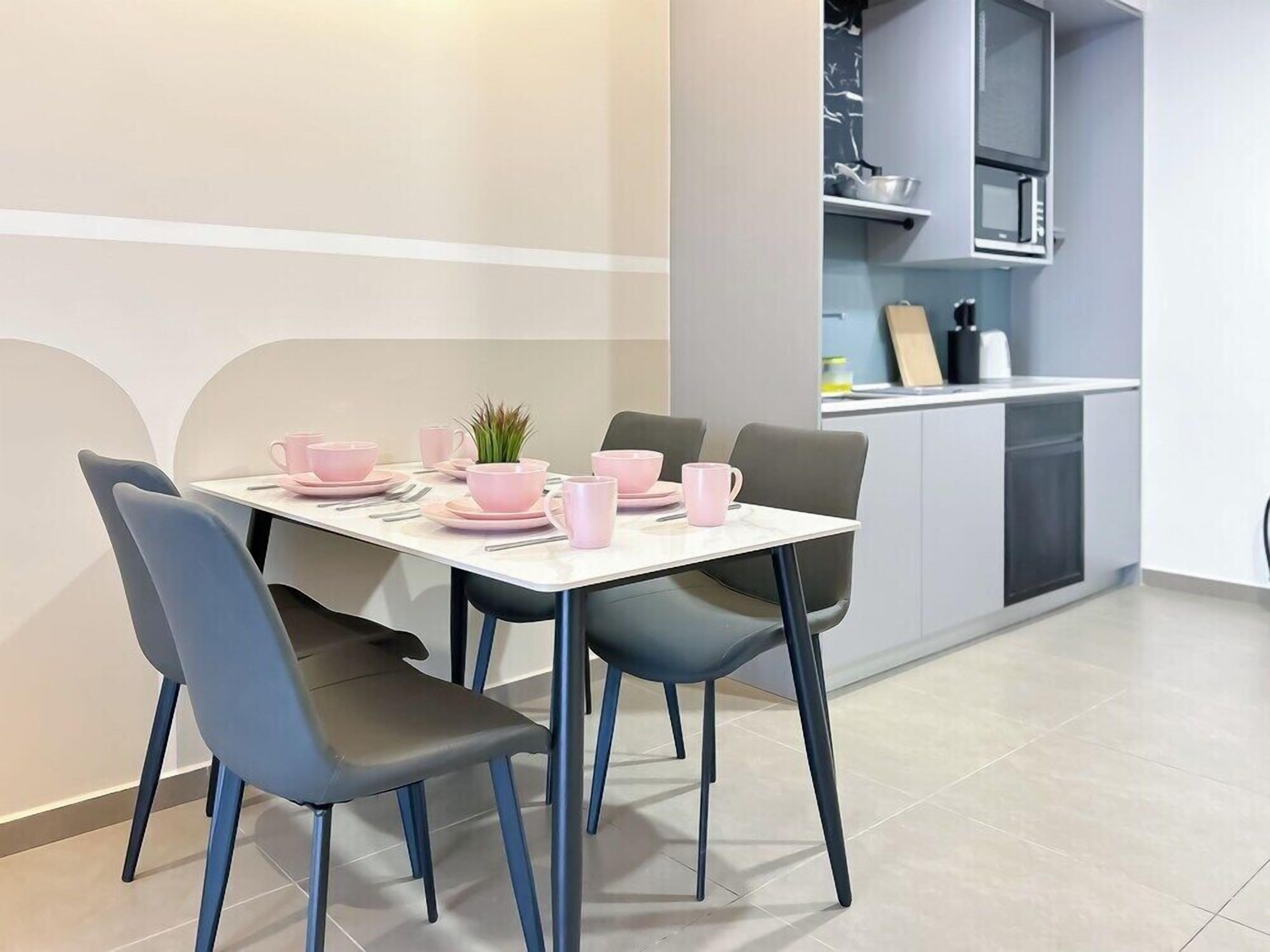 A modern dining area with a white table set for four, grey chairs, and pink tableware.