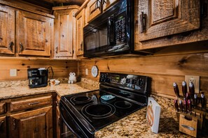 A kitchen with wooden cabinets, a black microwave, a stove, and a coffee maker. - Owls and Friends - 3 King Bedroom with ensuites-Hot tub-Pool Table (Blue Ridge)