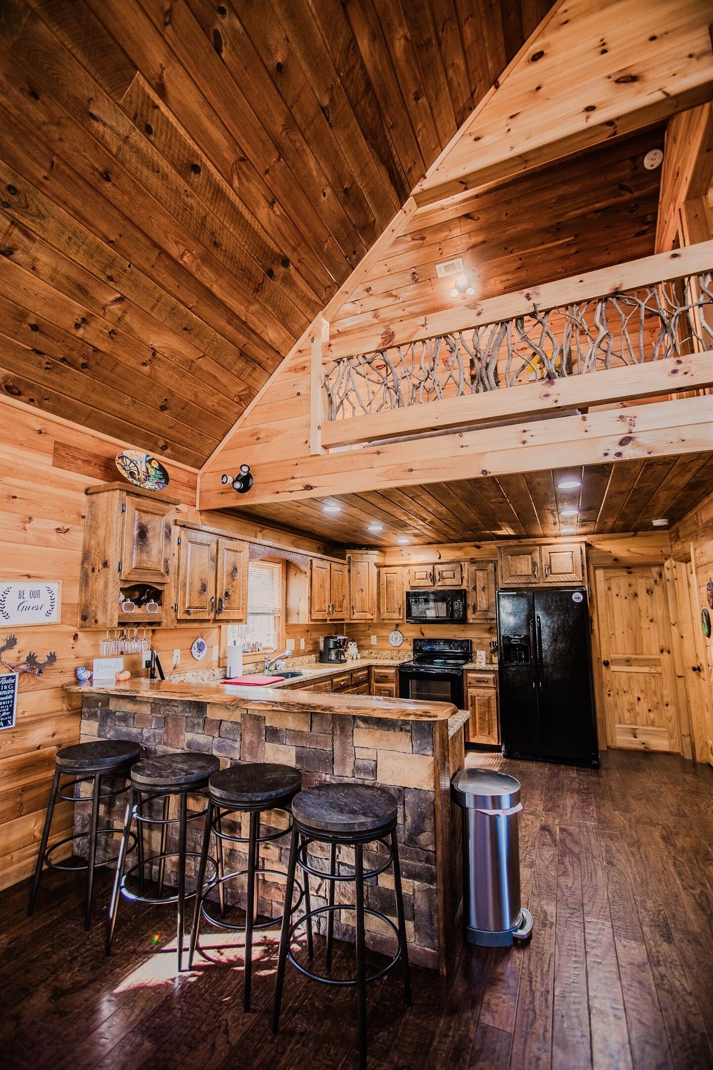 A wooden cabin interior with a kitchen, bar area, and a loft space.