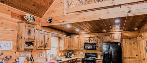 A wooden cabin interior with a kitchen, bar area, and a loft space.
