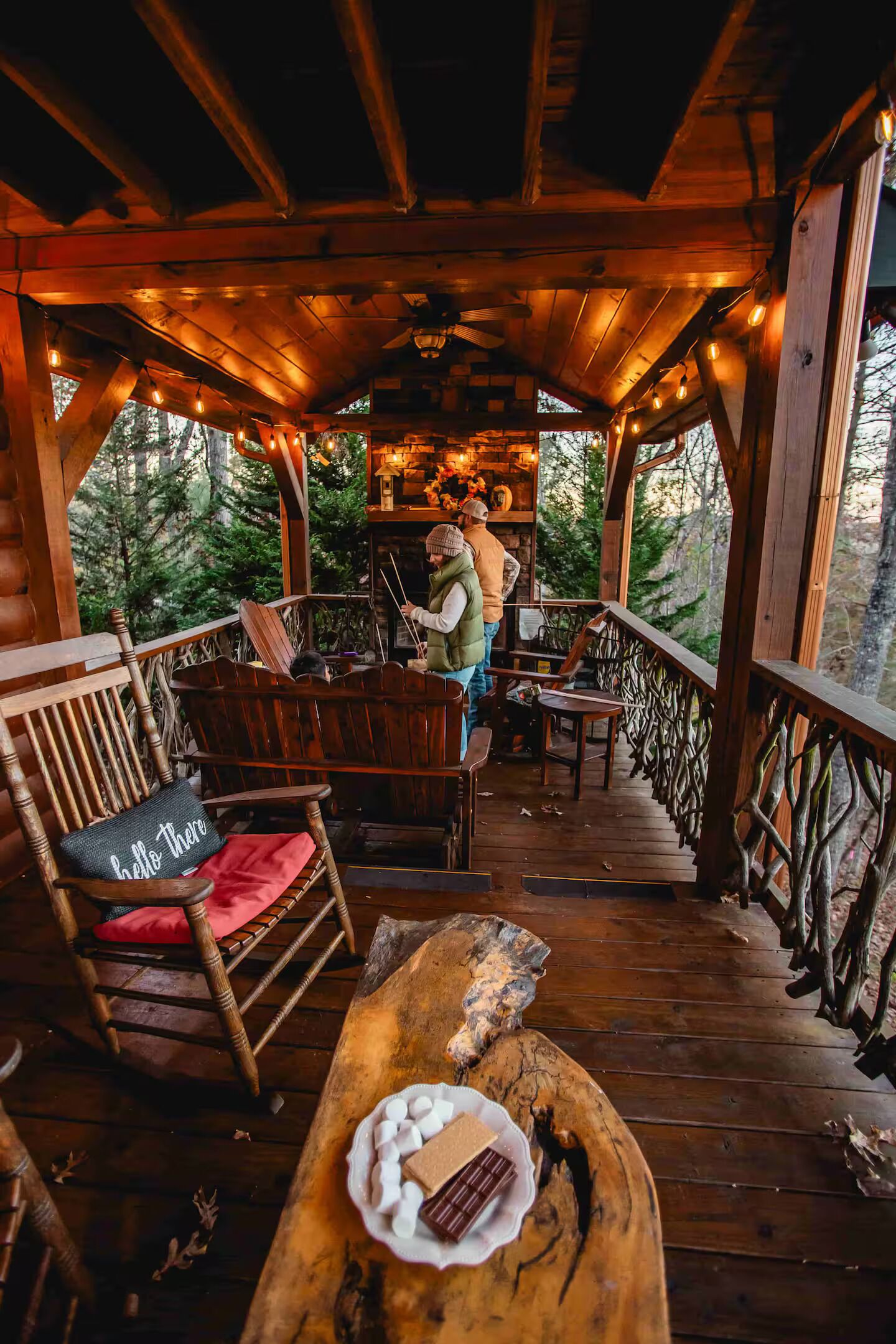 Een houten terras met rustieke meubels, een open haard en uitzicht op het bos.